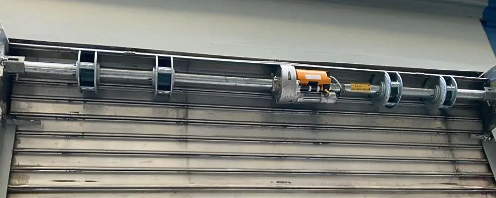 Installation d'un moteur central sur l'axe d'enroulement d'un rideau métallique pour une motorisation à Paris 18